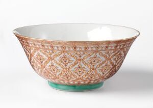  A traditional Bencharong porcelain bowl with a terracotta and green base, adorned with white, orange, and green symmetrical floral patterns and gold gilding, set against a plain background. Artist name and title unknown.