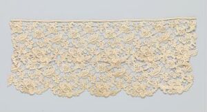  An off-white, vintage-style lace fabric with a scalloped edge and an intricate floral pattern, displayed against a light grey background.