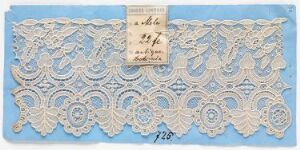  An intricate white lace fabric with a symmetrical pattern of floral and paisley designs against a light blue background, with a handwritten tag positioned in the center of the lace.