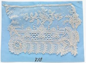  A delicate white lace fragment with intricate floral and geometrical patterns displayed on a calm blue background, with the handwritten annotation "£10" at the bottom right corner.