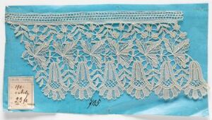  An intricately designed piece of white or cream lace fabric displayed on a light blue background, with an attached label suggesting that it might be part of a collection or sale.