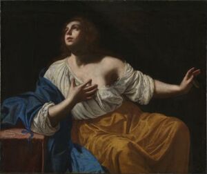  "Mary Magdalene Penitent" by Artemisia Gentileschi, depicting Mary Magdalene in an emotional state of spiritual seeking. She is seated with her body turned to the right, gazing upwards with a hand raised and the other touching her chest. She wears a loose white blouse and golden-yellow skirt with a blue cloak resting on her lap. The background is dark, emphasizing the strong contrast of light and shadow on her figure.