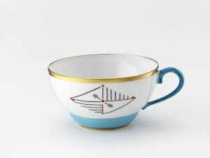  A white porcelain teacup with gold rimming on top, a sky blue band around the middle showcasing a minimalistic blue sailboat design, and a blue handle, all against a plain white background.