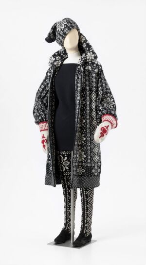  "Conte Nordique nr 1", a fashion design by Per Spook, showcasing a mannequin wearing a traditional Nordic-inspired black and white patterned coat, matching leggings and boots, adorned with pink embroidered mittens and a patterned headpiece, all set against a white background.