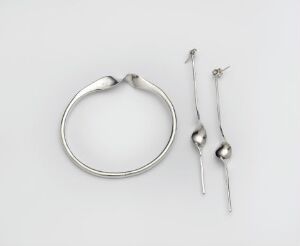  A silver fibula by Tone Vigeland, featuring a circular shape with undulating edges connected to two spikes with rounded terminals, displayed on a white background, displaying the craftsmanship of design and metalwork.