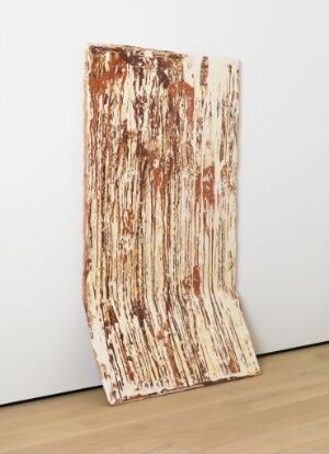  A ceramic artwork titled "Panel, resting/standing II" by Marit Tingleff, featuring a large, free-standing clay panel with a light beige base and decorated with various rich browns, deep oranges, and dark accents. The panel leans against a white wall on a light wooden floor, displaying an organic and earthy appearance with a glossy finish from the transparent glaze.