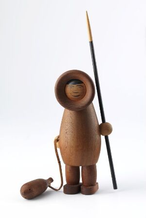  Stylized sculpture titled "Mann med harpun og sel" by Arne Tjomsland, featuring a brown teak wood figure holding a black harpoon with a separate small seal object, both on a plain white background.