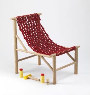  "Knut" by Jette Graaner, a modern design chair with a light oak wood frame and a vibrant red woven synthetic fiber seat, accentuated with playful yellow and red elements at the base.