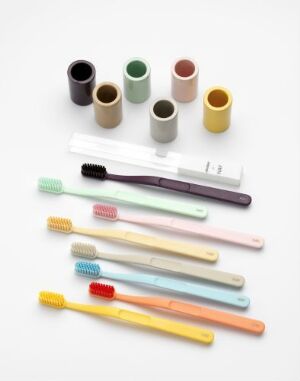  A collection of designer toothbrushes and holders by Andreas Engesvik titled "Tann", featuring toothbrushes with pastel-colored handles in front of cylindrical toothbrush holders in muted matte colors, arranged on a white background.