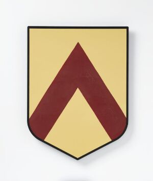  Shield-shaped object with pale yellow background and a centered chevron symbol in a deep reddish-brown, displaying a stark, minimalist design. Artist name: unknown. Title: Initiativ teller.