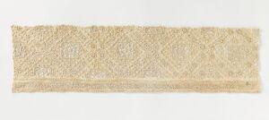  Image of a long, creamy beige piece of lacework with a complex, interconnected pattern, displayed against a pale neutral background. Artist name and title remain unknown.