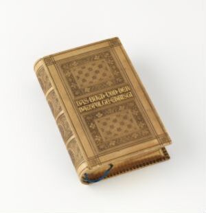  An antique book titled "Das Buch von der Nachfolge Christi" bound in tan calf leather with pressed ornaments and gold lettering on the cover, alongside gilded page edges, resting on a light background.