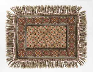  An intricately patterned rectangular textile, with a floral motif central panel in shades of red and green, surrounded by a series of decorative borders and a light beige tassel fringe.