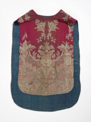  Antique sleeveless garment with a burgundy central panel featuring a detailed floral pattern in cream, beige, and muted green, bordered by a plain blue-grey fabric giving a denim-like appearance, presented against a neutral background. The overall shape resembles a shield, and the fabric shows signs of age and use. Artist name and title are unknown.