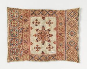  A rectangular handwoven rug or tapestry with fringes featuring a beige center with symmetrical reddish-brown and blue floral motifs surrounded by complex geometric borders in shades of brown, orange, blue, and white.