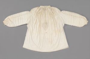  An off-white vintage child's blouse with long sleeves, ruffled collar, and cuffs laid flat on a light gray background.