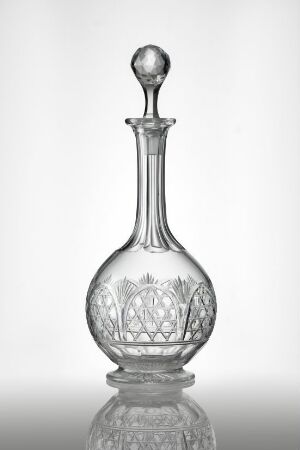  A clear glass decanter with a bulbous base, intricate cut glass patterns, and a matching stopper against a gradient grey background.