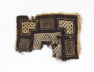  A fragment of aged, cream-colored textile with symmetrical black or dark brown geometric patterns, featuring squares and rectangles with intricate internal designs, set against a plain background. The fabric is frayed and appears antique.