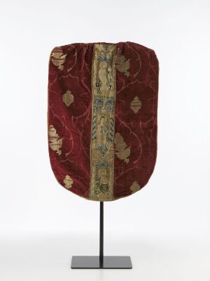  An antique deep red textile with faded golden patterns and a central embroidered stripe featuring a light background and colorful designs, mounted on a modern display stand against a plain backdrop.