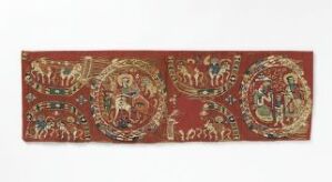  An antique, narrow textile with symmetrical, intricately detailed medallions and patterns in muted gold, green, and tan on a dark red background, possibly of historical or cultural significance.