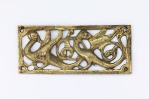  A cast and gilded copper-based metal plate with openwork floral design by an unidentified artist titled "Beslag". The plate exhibits a golden color with a detailed relief pattern and shows signs of wear, adding character to the intricate engravings and organic motif.