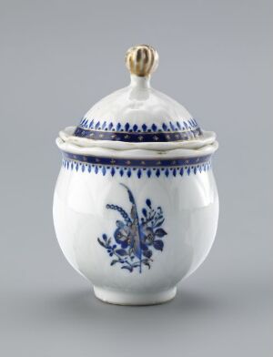  A small white porcelain container with blue floral patterns and a gold-toned knob on the lid, set against a light gray background.