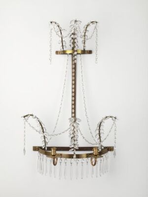  An ornate chandelier with two tiers of arms, the upper forming inverted arches draped with crystal beads and the lower supporting candle-like light holders, adorned with teardrop crystal pendants against a light background.