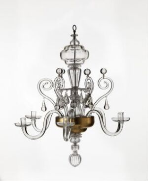  An ornate metal chandelier with sweeping arms, decorative elements, and a shiny silver finish, suspended against a plain, light-colored background.