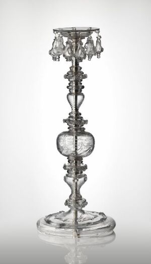  A transparent glass candle holder with an ornate baroque design, featuring a twisting stem and a spherical center, culminating in a crown-like arrangement with arms for holding candles, set against a light background. Artist name and title are unknown.