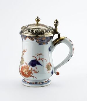  An intricately designed porcelain mustard pot with a metallic lid featuring a lace-like pattern, adorned with a colorful floral motif in cobalt blue, oranges, and greens, and a gold-accented handle.