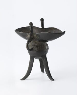  A sculpture with dark gray-black metallic tones, featuring three curvy legs, a rounded central body, a flat lid-like top with two vertical protrusions, set against a light grayish-white background.