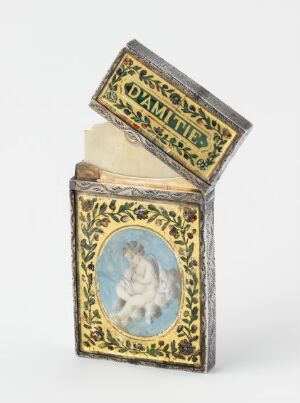  An antique-style decorative box with a black base color and gold detailing, displaying an oval illustration of a cherub at the front, and an interior lid labeled "DYNAMITE" in gold on black, containing paper items.