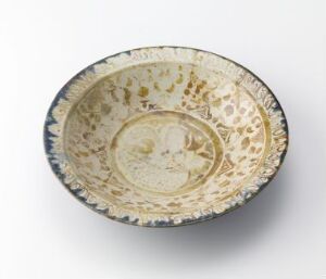  An antique-looking bowl with elaborate gold and possibly silver or white decorative patterns, including a central motif, speckled sections, and a rim with a contrasting darker pattern, set against a plain background.