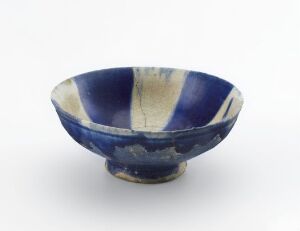  A small footed ceramic bowl with a deep cobalt blue exterior and a lighter blue-to-tan interior featuring a vertical drip glaze pattern. The bowl's rim is uneven, suggesting a handmade quality.