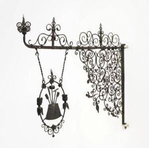  A black wrought iron bracket titled "Oppheng for håndverkerskilt" by an unknown artist, featuring Baroque-inspired scrollwork with a horizontal bar and a hanging sign decorated in a similar ornate style against a white background.