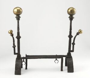  An iron "Kaminbukker" with brass spheres, consisting of a robust horizontal base with upward extending supports and decorative spheres on top, set against a light gray background.