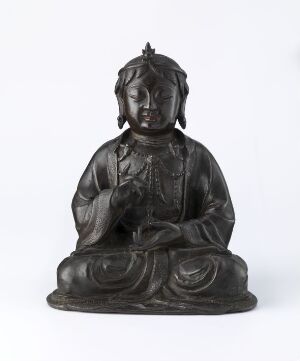  A dark-toned bronze statue of a seated figure in a meditative pose with an elaborate headpiece and robes, classically identified as a deity in Buddhist culture, against a light background. Artistname and title are unknown.