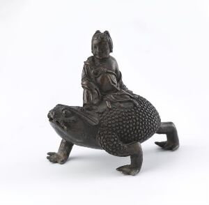  A metallic dark bronze figurine of a person riding a large toad, both depicted in a monochromatic color scheme against a plain light gray background.