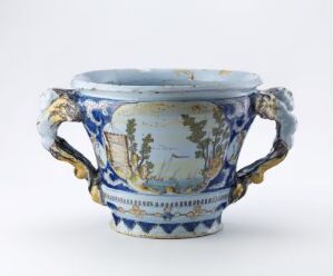  An ornate blue and white ceramic jardiniere with golden accents and detailed landscape paintings on the body, and handles designed to resemble twisted branches.