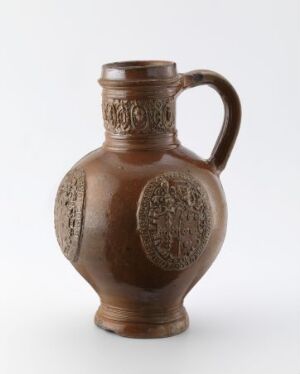  A spherical brown ceramic jug with a single handle and embossed medallion designs on the sides, set against a neutral background.