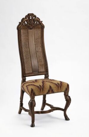  An ornate chair made from walnut ("Nøttetre"), with a carved high backrest featuring a rattan panel, and a plush velvet seat in a patterned fabric. The chair legs are elegantly carved with connecting crossbars for stability. It is a traditional piece titled "Stol" by an unknown artist.