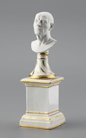  A classical Fürstenberg porcelain bust depicting a man's head and neck in matte white, set on a pedestal with a glossy finish and gold accents, showcasing a contrast between the unglazed porcelain and the ornate, gilded detailing.