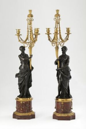  A pair of classical-style candelabras with dark bronze-like female figures serving as the base, supporting elaborate golden arms designed to hold candles, mounted on decorative gilded bases.