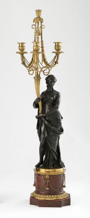  A tall, slender bronze candelabrum with a dark classical figure at the base on a lighter brown and gold-trimmed round stand. The candelabrum has symmetrical, curving golden arms extending upward to hold candles.