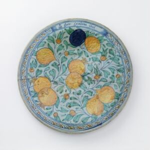  A decorative ceramic plate featuring a lush pattern of yellow lemons and green leaves on a muted blue background, surrounded by a dark blue border adorned with white and green floral motifs.