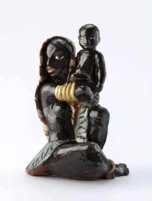  A glossy, dark-colored statue of an adult figure seated on the ground with a child figure on its lap, with light bands around the adult's wrists and greenish leaf-like details at the base.