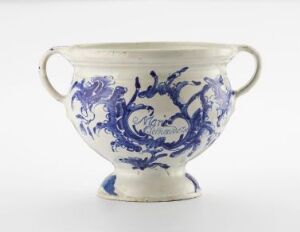  A two-handled ceramic skyphos with a creamy white base color, featuring vibrant cobalt blue floral and scrollwork patterns, against a plain white background.