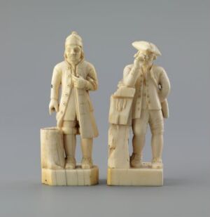  Two carved ivory figures by artist Jørgen Garnås titled "Mann fra Mandal," depicting men in historical European clothing with canes and tricorn hats, displayed against a gray background.