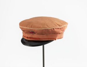  "Norges første russelue" by Hans H Holm a/s, a traditional student cap with a light brown satin-finish cotton body and a shiny black lacquered brim, decorated with a braided cord.