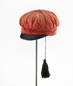  A traditional Norwegian "Russelue" student cap by artist Hans H Holm a/s. The cap is made of machine-woven red cotton satin with a glossy black visor, decorative silk cord, and a tassel hanging from the right side.